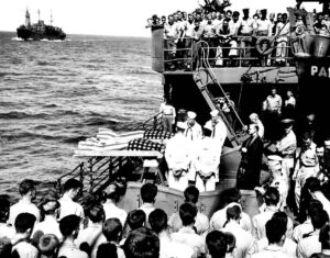 Doi soldați înrolați pe nefericitul portavion LISCOME BAY, torpilat de un submarin japonez în Insulele Gilbert, sunt îngropați pe mare de pe puntea unui transport de asalt echipat de Garda de Coastă.